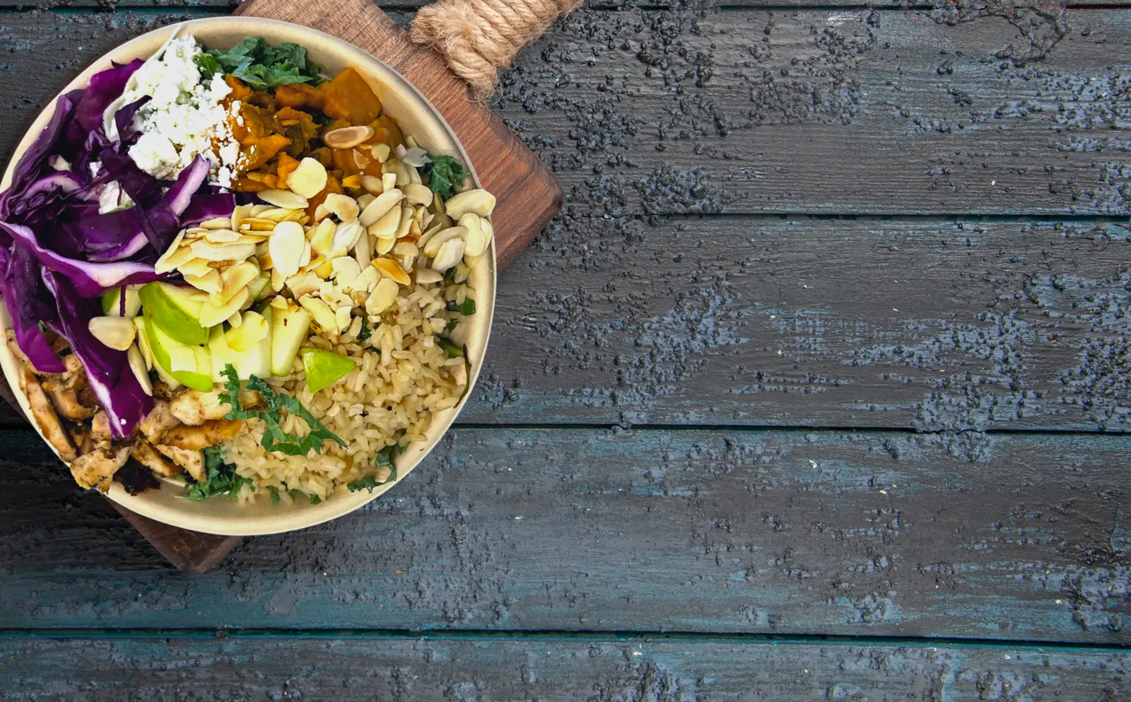 Warm bowl of roasted sweet potatoes, green apple, red cabbage and toasted almonds over brown rice